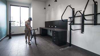 A man is holding a bike in a room with a desk and a bike rack